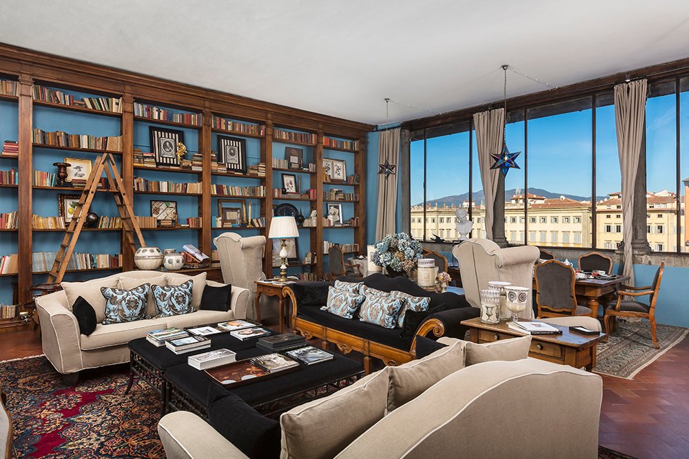 Bright and airy Florence villa living room with designer furniture, classic fireplace, neutral-toned armchairs, and open double French doors leading to a lush private garden.